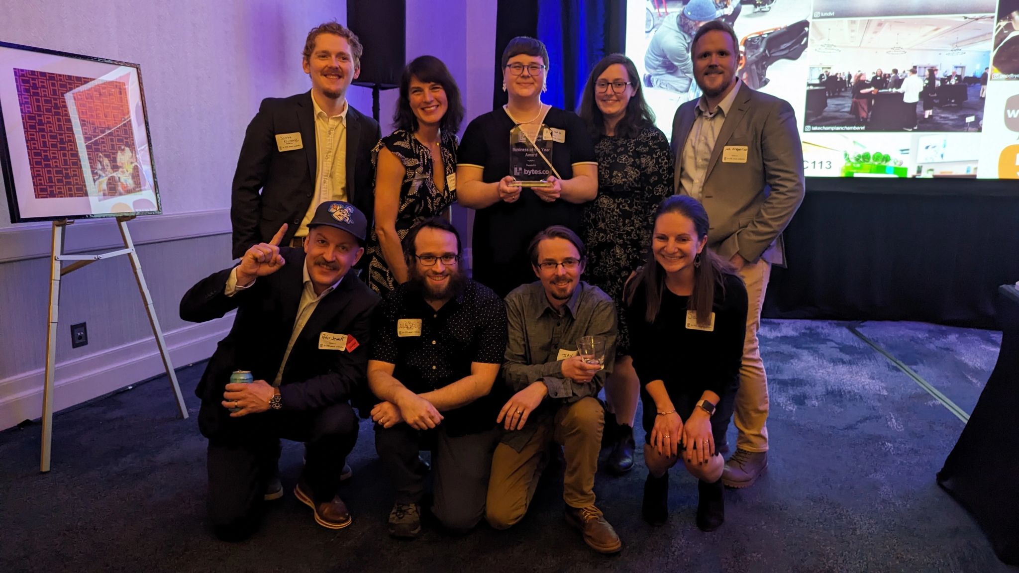 The Bytes.co team standing and kneeling together for a group photo after accepting the Lake Champlain Chamber 2024 Business of the Year award. From left to right: Scott Kliczewski, Kristina Drobny, Hannah Hook, Lilly Romano, Josh Kirkpatrick, Peter Jewett, Aaron Silber, Jay Di Vece, and Sarah Maines.